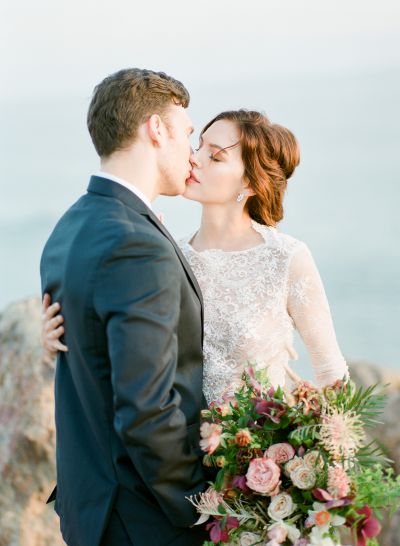 A bride kisses her groom and holds a bouquet by Lavenders Flowers